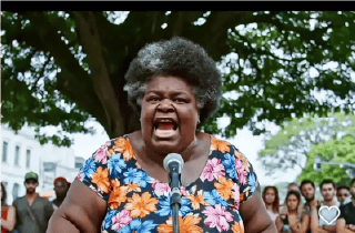 Woman wearing colorful dress yelling into a microphone in front of a crowd