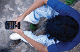 Overhead image of a boy with dark hair sitting on the ground looking at his smartphone