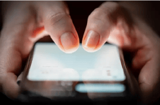 Two thumbs operating a lit up smartphone screen